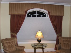 custom cornice over arch window with tied back drapery panels and contrast reupholstered chairs