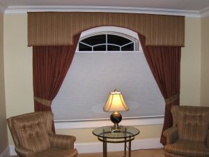 Custom cornice over arch window with tied back drapery panels and contrast reupholstered chairs